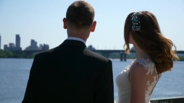 Gelin ve damat nehir kenarında yürüyor. Düğün günü. Şehir manzarası Şehir Sahnesi. 2x Yavaş çekim - 0.5 Hız 4K 60 FPS