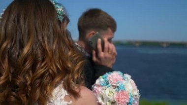 Gelin ve Çiçek Buketi, Damat Akıllı Telefonda Sohbet Ederken Bekliyor. Şehir manzarası arka planı. 2x Yavaş çekim - 0.5 Hız 60 FPS 4K