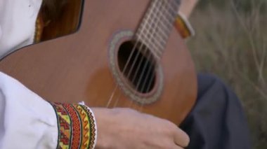 Yakın plan Müzisyen Saha Arasında Otururken Gitar Üzerinde Çalıyor. 4K HDR