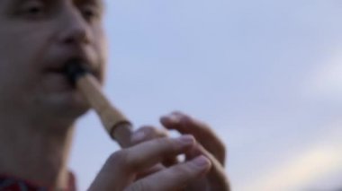 Yakın plan Müzisyen Tarlada Otururken Ahşap Flüt Çalıyor. 4K HDR