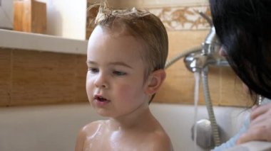 Çocuk Küvette Banyo Yapmayı Seviyor. Anne, çocuğu banyoda yıkıyor. 2x Yavaş çekim 60 fps