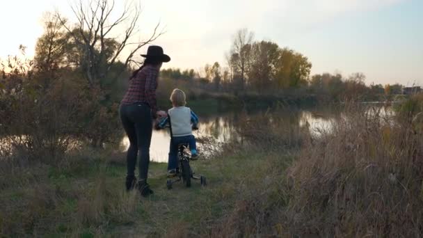 Matka a syn Pěší túra na kole u řeky. Dítě objevuje světovou matku vypráví o přírodním prostředí. Západ slunce nad venkovskou scénou. Zpomalený pohyb
