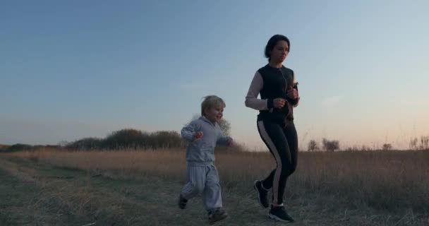太陽の前のフィールドロードでジョギングを実行している母と息子 朝の日の出 サンセットライティング — ストック動画
