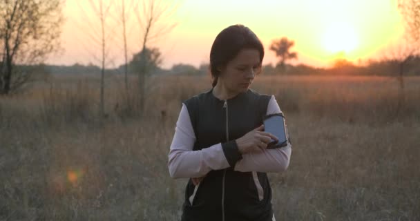 女手指在智能手机上启动秒表 年轻女子在大自然的晨曦中奔跑 — 图库视频影像