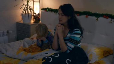 Anne ve Çocuk Yatmadan Önce Yatakta Dua Ediyor. Noel arifesi yatak odasında. Yeni yıl tatilleri. 4K 2x Yavaş çekim 60 fps