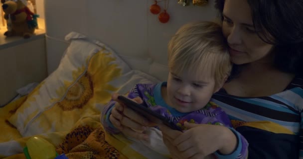 엄마와 아이는 침대에 스마트폰으로 비디오를 침실에서 크리스마스 — 비디오