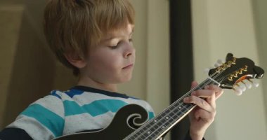 Beyaz çocuk evde Mandolin oynuyor. Avrupalı Çocuk Müzik Çalışması 4K 10-bit