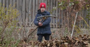 Boy Rakes Arka Bahçede Yapraklar. Soğuk Sonbahar Havası Ağır çekim 4K 10-bit 