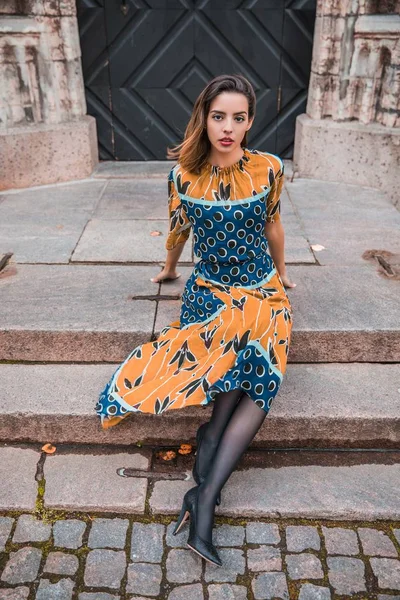 Güzel, sıska Arnavut kız poz veriyor ve turuncu mavi süs elbisesini gösteriyor