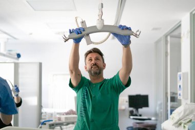 Nurse wearing gloves installing a patient lift in a hospital room, preparing to move or lift a patient
