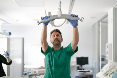 Doctor wearing blue gloves installing medical lifting equipment in hospital room