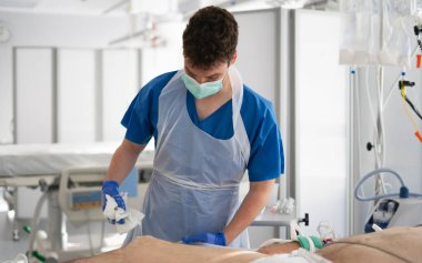 Nurse wearing personal protective equipment carefully cleaning patient's skin during medical procedure in hospital room