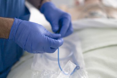 Surgeon preparing catheter tube while a patient lies in the background in a hospital operating room