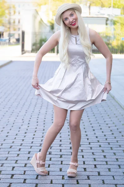 Emotional girl in a dress and hat posing holding the hem of the dress