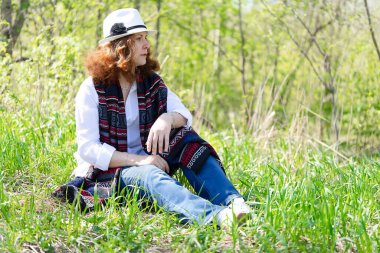 Parktaki çimlerin üzerinde oturan kızıl saçlı bir kadının portresi.