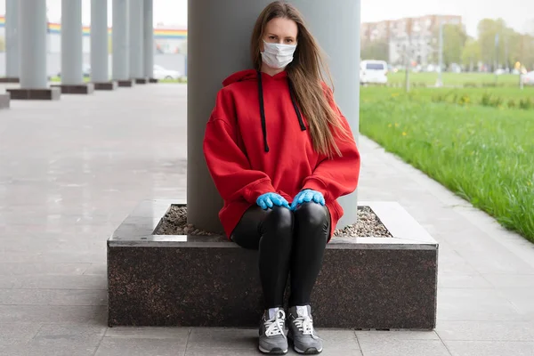Portrait of a girl sitting by the column. Wearing a medical mask and gloves
