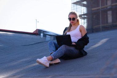 Dizüstü bilgisayarda çalışan güzel sarışın. Güneşli bir günde bir evin çatısında.