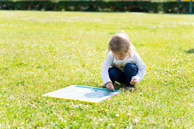 Küçük kız doğada tahtaya tebeşirle çizer. Yaz güneşli