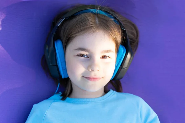 Küçük kız, mor bir halıda duran kulaklıkla müzik dinliyor.