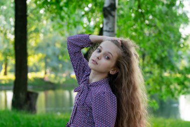 Parktaki küçük bir kızın portresi çimenlerin, ağaçların ve gölün arka planında.