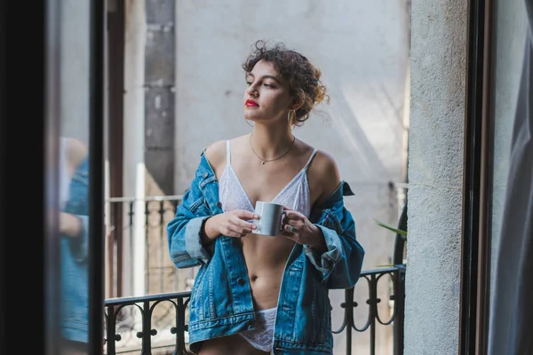Woman in denim jacket holding cup on balcony — Stock Photo, Image