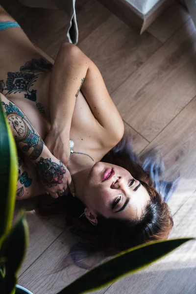 官能的な刺青女性の胸をカバーし 木材の床に横たわっている間首に触れる — ストック写真