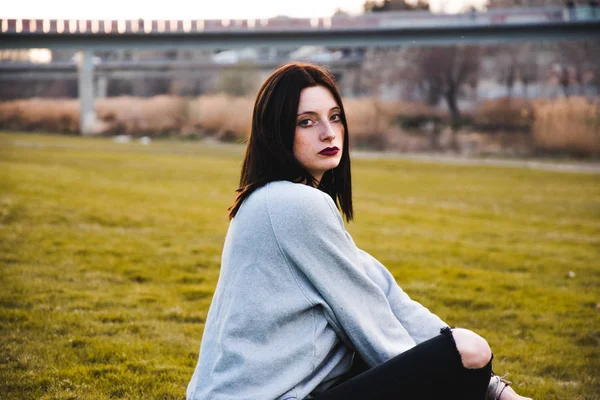 Alvorlig Brunette Afslappet Outfit Med Mørk Makeup Sidder Grønt Græs - Stock-foto