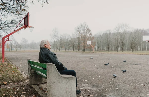 Oudere Man Leren Jas Zittend Bank Buurt Van Sportveld Park — Stockfoto