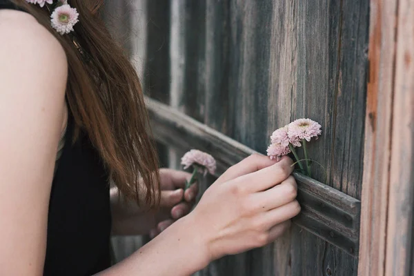 田舎の家のみすぼらしい木の壁にきれいな花を入れて認識できない女性 — ストック写真