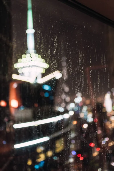 Размытый Вид Ярко Освещенный Современный Город Через Мокрое Стекло Дождливую — стоковое фото