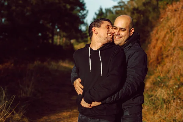 欢快的同性恋夫妇拥抱在森林的走道在阳光明媚的一天模糊的背景 — 图库照片