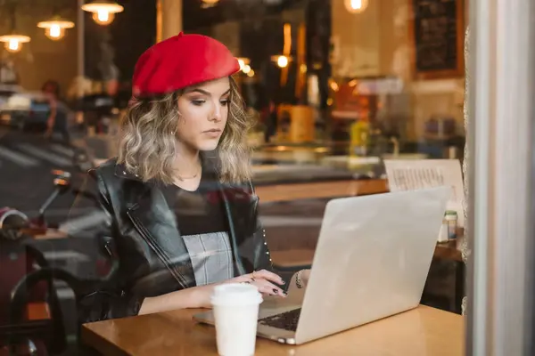 Молодая Женщина Красном Берете Горячим Напитком Ноутбуком Сидит Кафе — стоковое фото