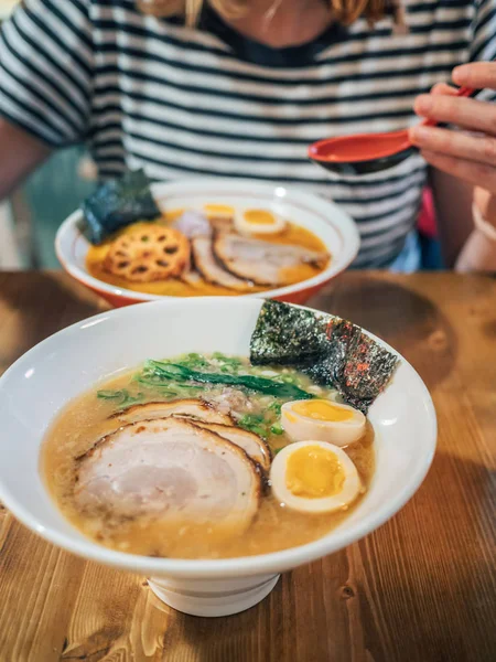 木製のテーブルに座り 卵とスライスした豚肉をトッピングした美味しいラーメンを楽しむ女性のトリミングされた眺め — ストック写真