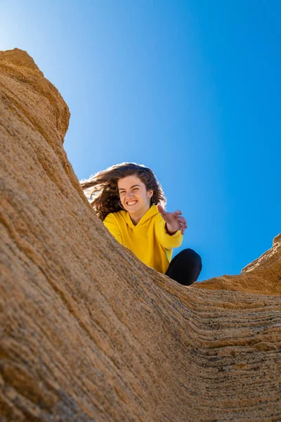 青空の背景に砂岩の岩に手を与える黄色のスウェットシャツのブルネットの女性の肖像画 — ストック写真