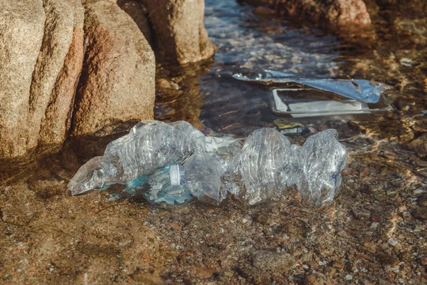 空空的塑料压扁瓶子废物躺在岩石附近的海滨清澈的水里 — 图库照片