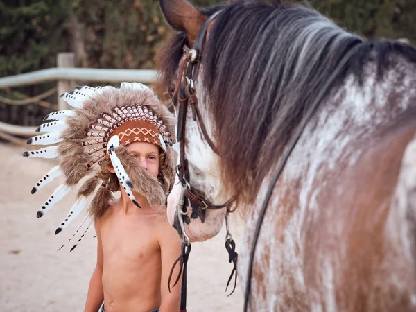 穿着印度羽毛战帽 带着马在农场里快乐的孩子 — 图库照片