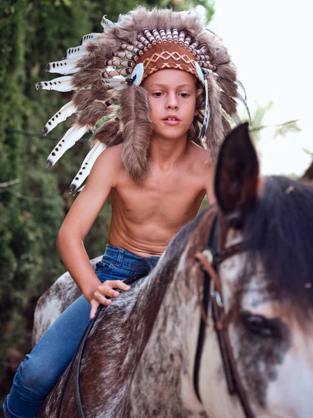 Серьезный Мальчик Настоящей Индийской Шляпе Перьями Верхом Лошади Парке — стоковое фото