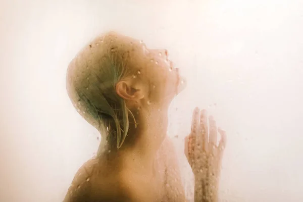 在浴室湿透的透明隔板后面洗澡的年轻女性侧视图 — 图库照片