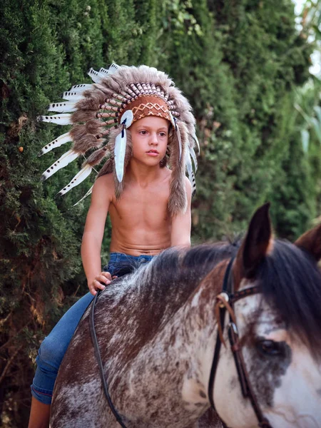 严肃的男孩 戴着正宗的印度羽毛帽 骑着马在公园里 — 图库照片