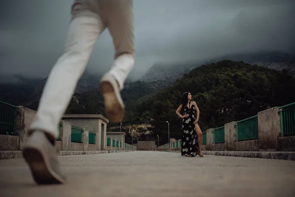 Hombre corriendo hasta la fecha con hermosa mujer de pie en vestido largo en puente de piedra — Foto de Stock