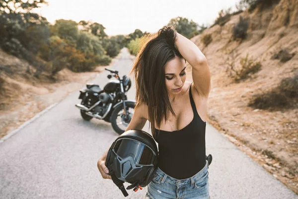 Mulher sedutora com capacete em pé ao lado motocicleta estacionada — Fotografia de Stock