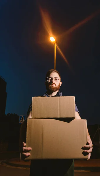 Человек Очках Несущий Коробки Стоя Улице Глядя Камеру Возле Светящегося — стоковое фото