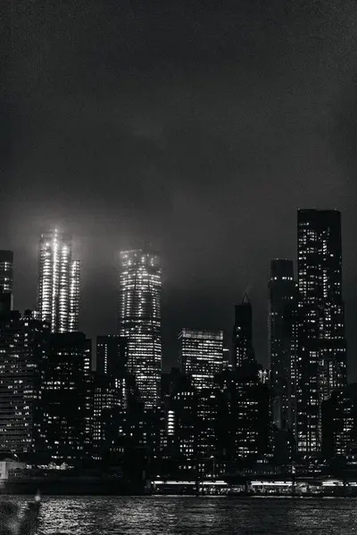 マンハッタンの近代的な照明スカイラインの黒と白の複合体は 夜の時間帯に穏やかな川の前に位置しています — ストック写真