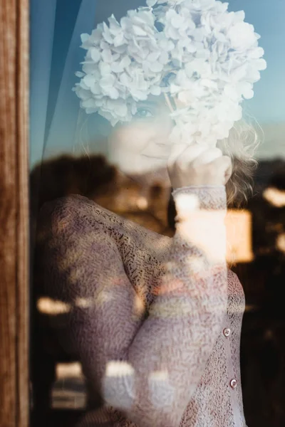 Улыбающаяся Женщина Уютной Одежде Стоящая Окна Закрывающая Лицо Цветком Гортензии — стоковое фото