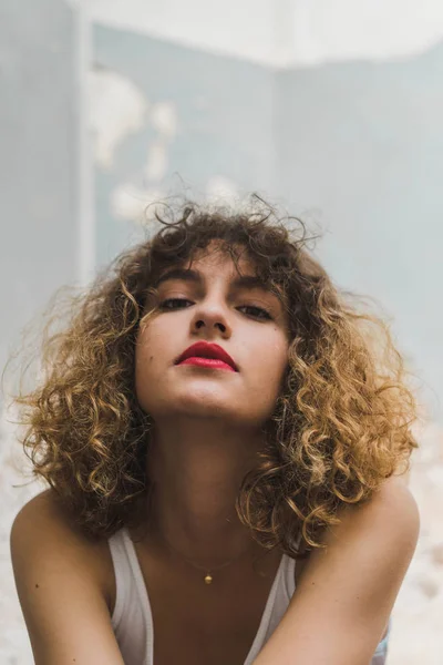 Primer plano de la joven mujer sin emociones con lápiz labial rojo y rizos voluminosos mirando a la cámara - foto de stock