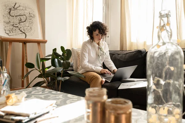 Mulher usando laptop perto desenha em papéis no sofá no quarto — Fotografia de Stock