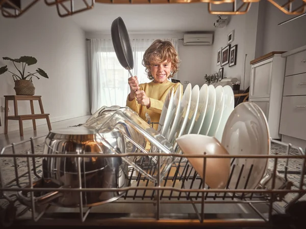 Pequeño niño molesto gritando mientras pone sartén en lavavajillas abierto en la cocina - foto de stock