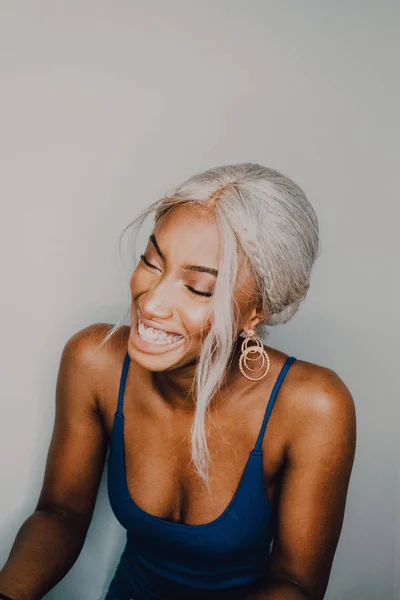 Cheerful adult African American female with blond hair wearing blue and closed eyes — Stock Photo