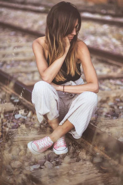 Femme aux cheveux longs assise sur des chemins de fer envahis d'herbe sèche — Photo de stock