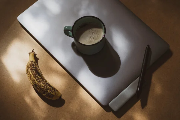 Taza de café en tableta gráfica con pluma y plátano maduro a la luz del sol - foto de stock